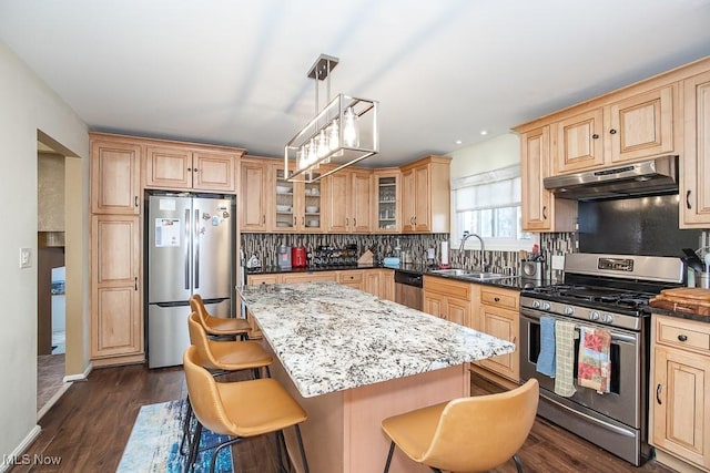 kitchen with light brown cabinets, a breakfast bar, a sink, under cabinet range hood, and appliances with stainless steel finishes