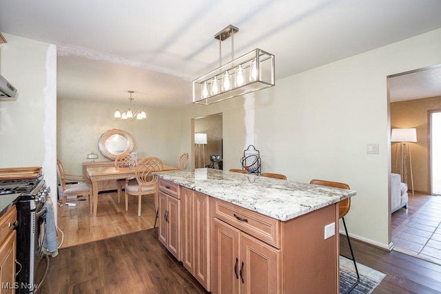 kitchen with light stone counters, dark wood-style flooring, a kitchen bar, stainless steel gas stove, and a center island