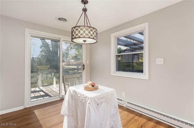 dining space featuring a baseboard heating unit, baseboards, visible vents, and wood finished floors