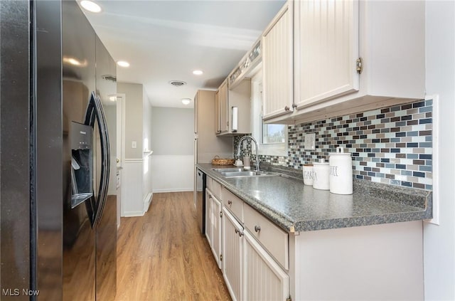 kitchen featuring visible vents, stainless steel dishwasher, light wood-style floors, black refrigerator with ice dispenser, and a sink