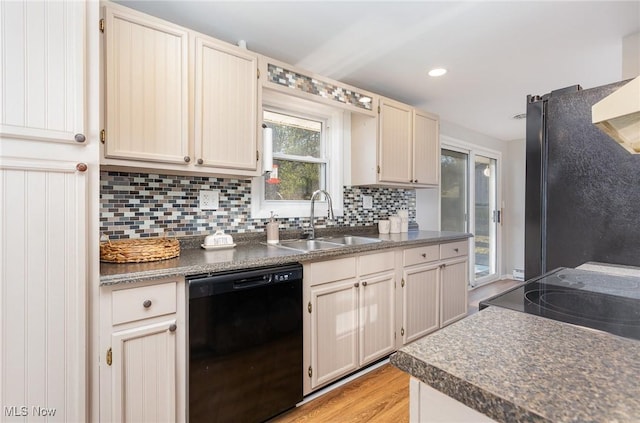 kitchen with tasteful backsplash, light wood finished floors, dark countertops, black appliances, and a sink