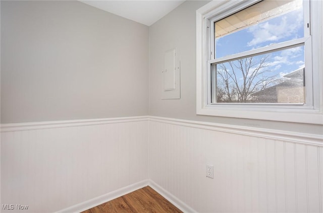 unfurnished room with wood finished floors and a wainscoted wall