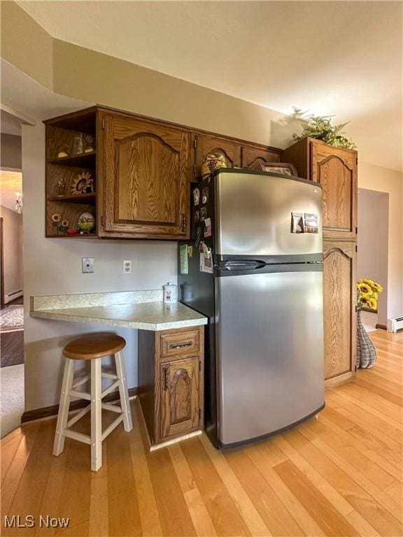 kitchen featuring light wood finished floors, open shelves, freestanding refrigerator, light countertops, and baseboard heating