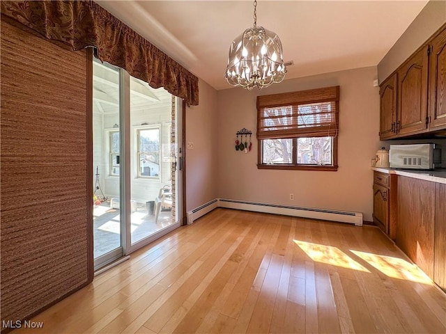 unfurnished dining area with an inviting chandelier, a healthy amount of sunlight, light wood-style floors, and baseboard heating