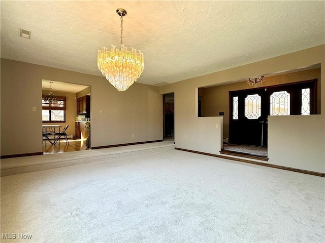 carpeted empty room with a textured ceiling, baseboards, and a chandelier