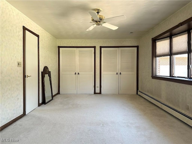 unfurnished bedroom with wallpapered walls, multiple closets, light carpet, baseboard heating, and a ceiling fan