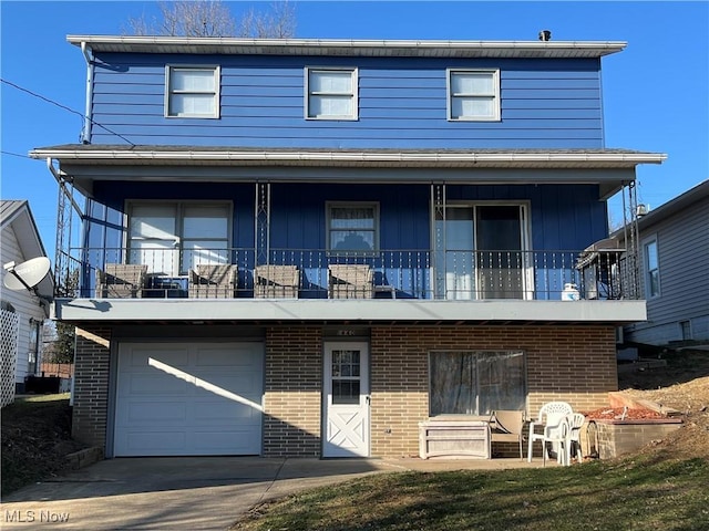 rear view of property with brick siding, driveway, an attached garage, and a balcony