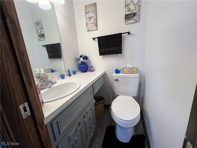 half bath with toilet, vanity, and wood finished floors