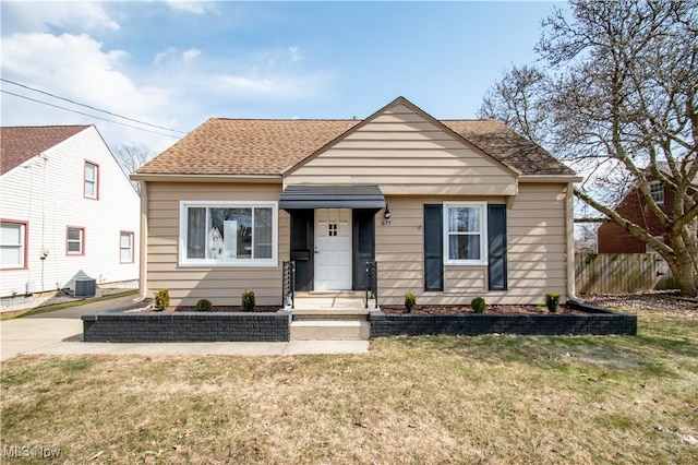 bungalow featuring a front lawn, central air condition unit, fence, and roof with shingles