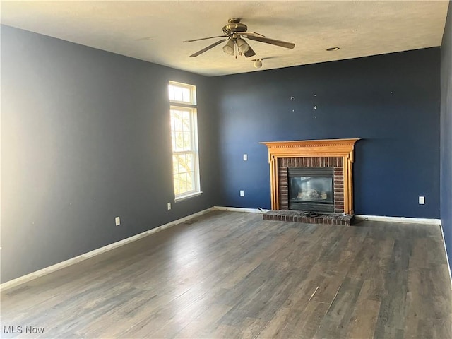 unfurnished living room featuring a brick fireplace, wood finished floors, baseboards, and ceiling fan