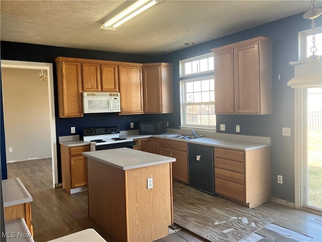 kitchen with a center island, light countertops, wood finished floors, black appliances, and a sink