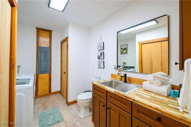 bathroom with toilet, electric panel, washer / dryer, wood finished floors, and vanity