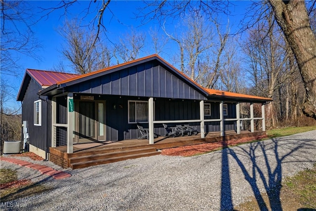 view of front facade with metal roof, covered porch, board and batten siding, and central AC