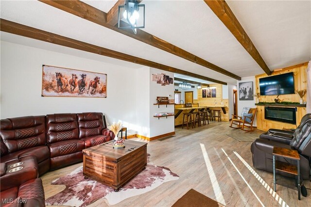 living area with a glass covered fireplace, baseboards, beam ceiling, and wood finished floors