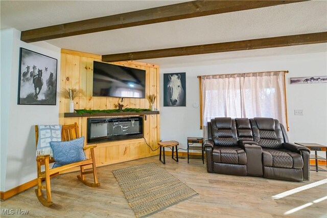 living room with beamed ceiling, wood finished floors, baseboards, and a glass covered fireplace