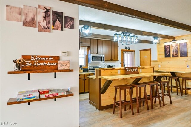 kitchen with wooden walls, beamed ceiling, a kitchen bar, light wood-type flooring, and appliances with stainless steel finishes