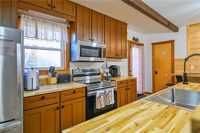 kitchen with beam ceiling, appliances with stainless steel finishes, wood counters, and a sink