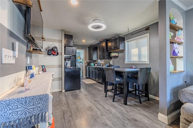 kitchen featuring light wood finished floors, backsplash, baseboards, light countertops, and black electric range