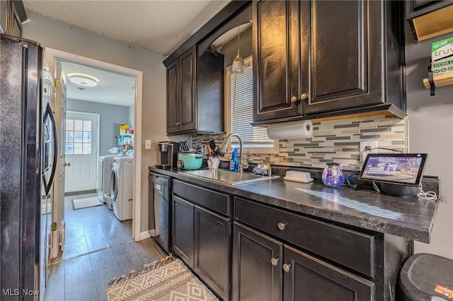 kitchen with dishwashing machine, a sink, dark countertops, washing machine and dryer, and black refrigerator with ice dispenser