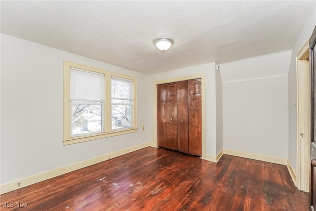 unfurnished bedroom featuring dark wood-style floors, baseboards, a closet, and a textured ceiling