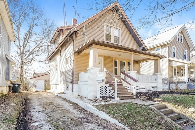 bungalow-style home featuring a porch, an outbuilding, aphalt driveway, and a chimney