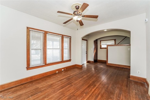 empty room with arched walkways, a ceiling fan, baseboards, and hardwood / wood-style floors