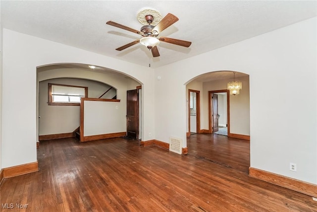 spare room featuring arched walkways, baseboards, and wood-type flooring