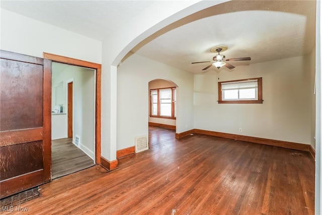 unfurnished room featuring visible vents, ceiling fan, baseboards, hardwood / wood-style flooring, and arched walkways