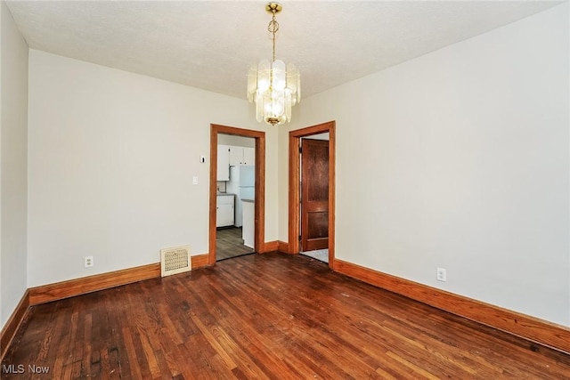 unfurnished room featuring a notable chandelier, visible vents, baseboards, and dark wood-style flooring