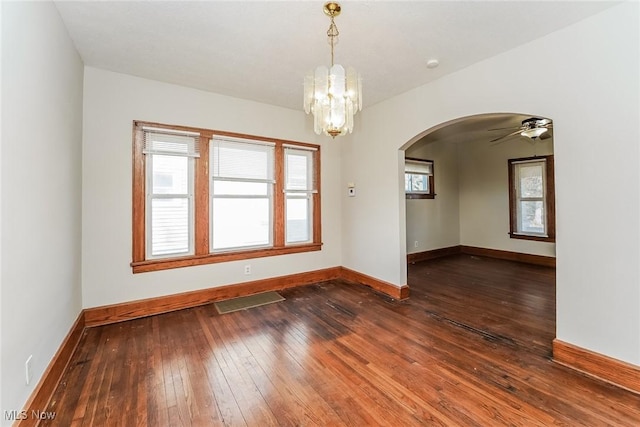 empty room with visible vents, arched walkways, baseboards, and dark wood finished floors