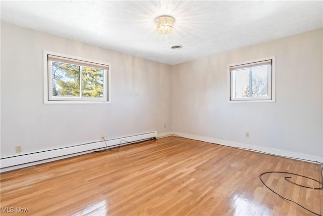 spare room featuring wood finished floors, visible vents, baseboard heating, and baseboards