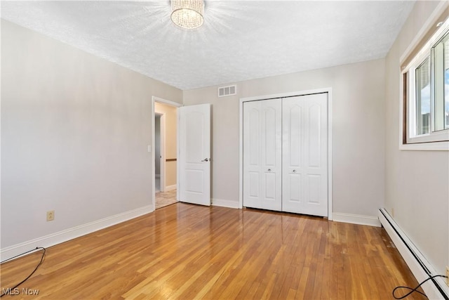 unfurnished bedroom featuring baseboards, visible vents, a baseboard radiator, light wood-style floors, and a closet