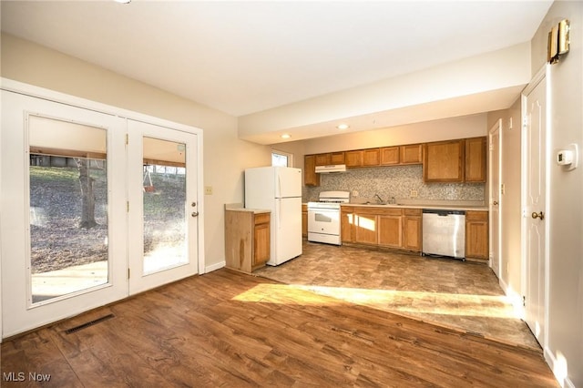 kitchen featuring white appliances, wood finished floors, visible vents, decorative backsplash, and brown cabinets