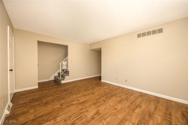 spare room featuring stairs, wood finished floors, visible vents, and baseboards