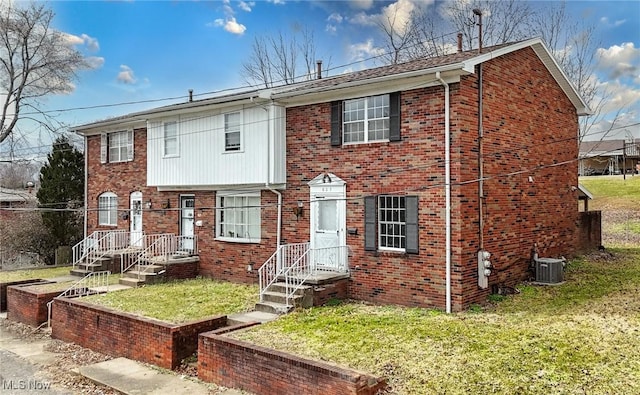 view of front facade featuring a front yard, brick siding, and central AC