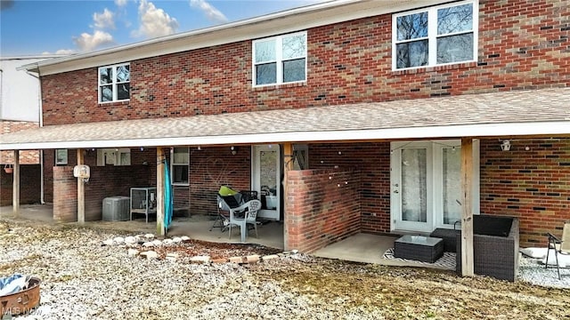 rear view of property with a patio, cooling unit, brick siding, and roof with shingles