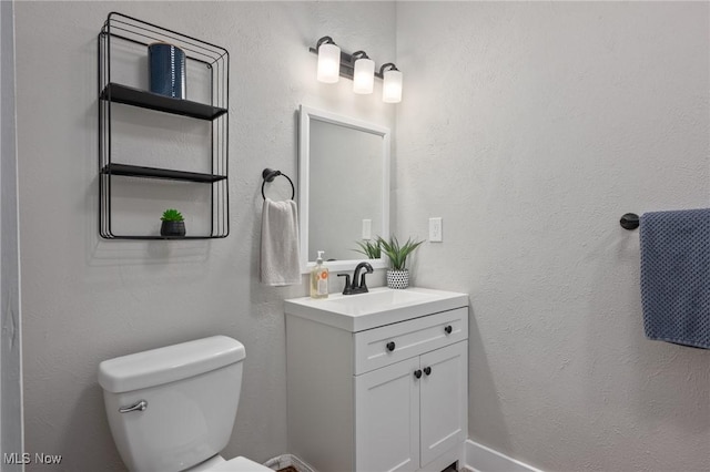 bathroom with toilet, vanity, and a textured wall