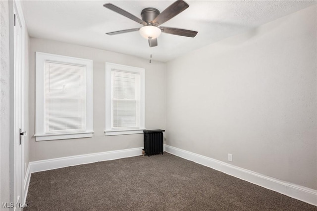 unfurnished room featuring radiator heating unit, baseboards, dark carpet, and ceiling fan