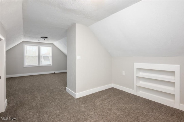 bonus room featuring lofted ceiling, built in features, a textured ceiling, dark carpet, and baseboards