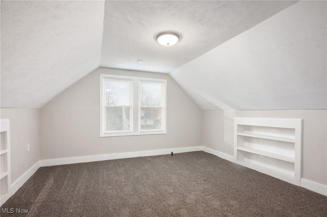 additional living space featuring baseboards, built in shelves, a textured ceiling, and carpet floors