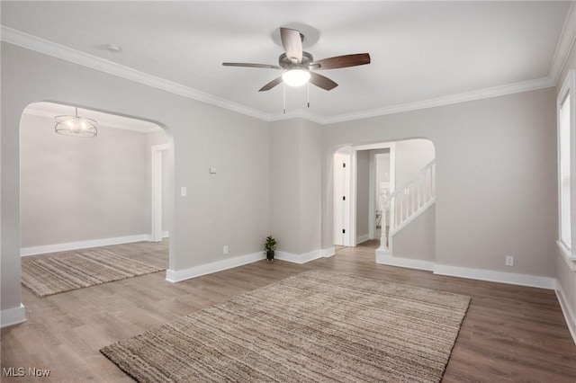 spare room with baseboards, arched walkways, wood finished floors, and ornamental molding