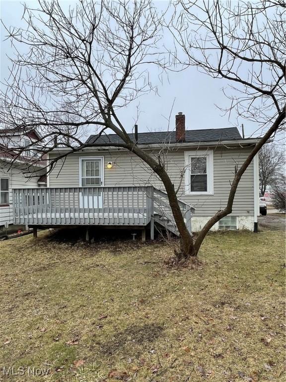 rear view of property featuring a lawn, a chimney, and a deck