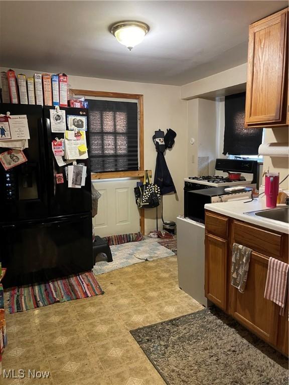 kitchen with brown cabinets, a sink, white gas range oven, light countertops, and black refrigerator with ice dispenser