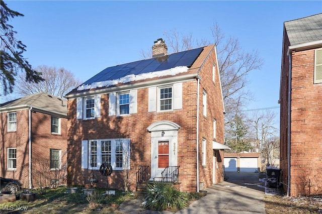 view of front of property with solar panels, a chimney, an outdoor structure, a garage, and brick siding