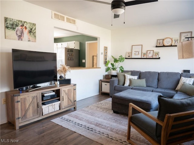 living room featuring a ceiling fan, dark wood-style floors, visible vents, and baseboards