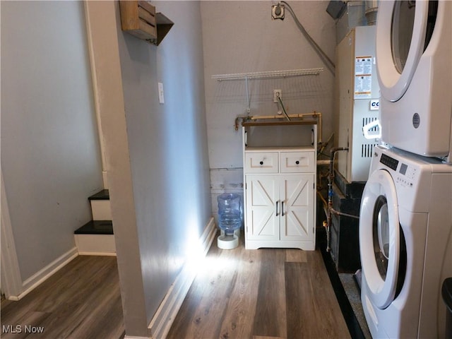 clothes washing area featuring laundry area, dark wood-style floors, stacked washer and clothes dryer, and baseboards