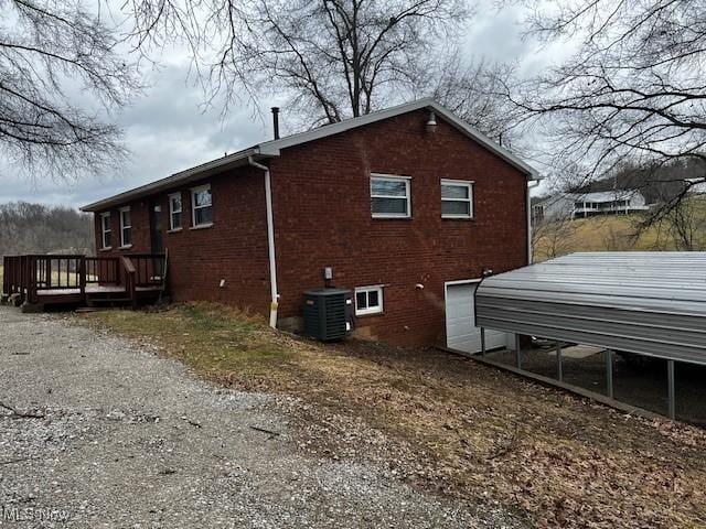 view of home's exterior with dirt driveway, brick siding, central AC, and a wooden deck