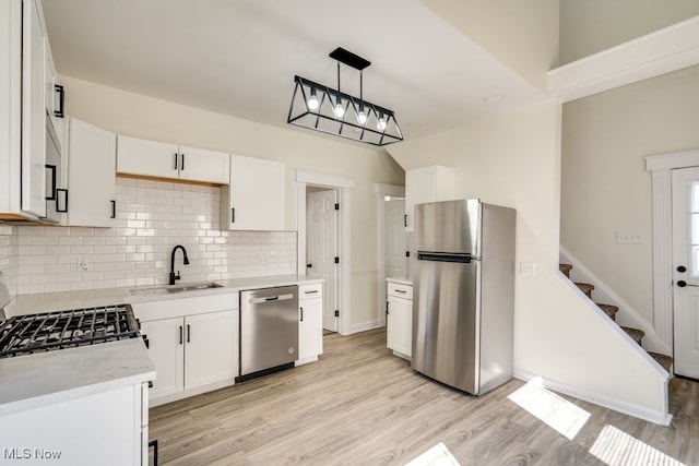 kitchen with light wood-type flooring, a sink, backsplash, appliances with stainless steel finishes, and white cabinets