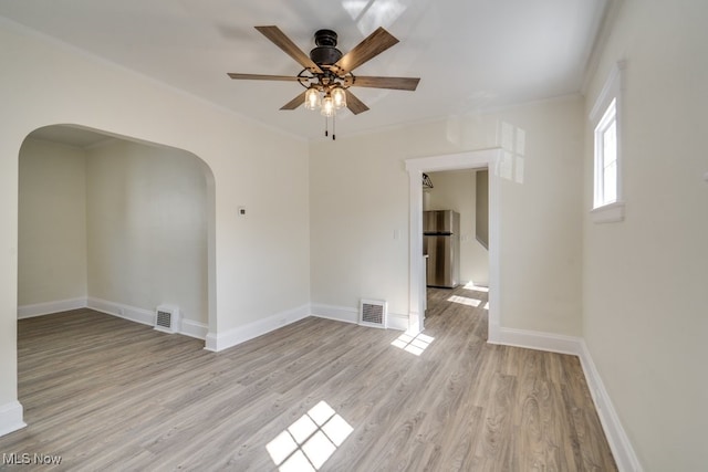 spare room featuring arched walkways, baseboards, crown molding, and light wood-style floors