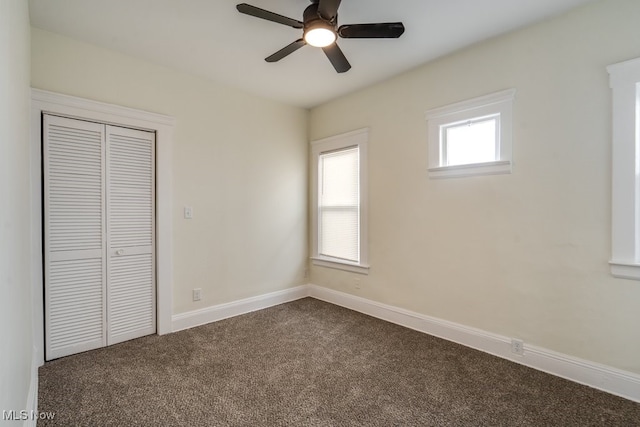 unfurnished bedroom with baseboards, dark colored carpet, a closet, and ceiling fan